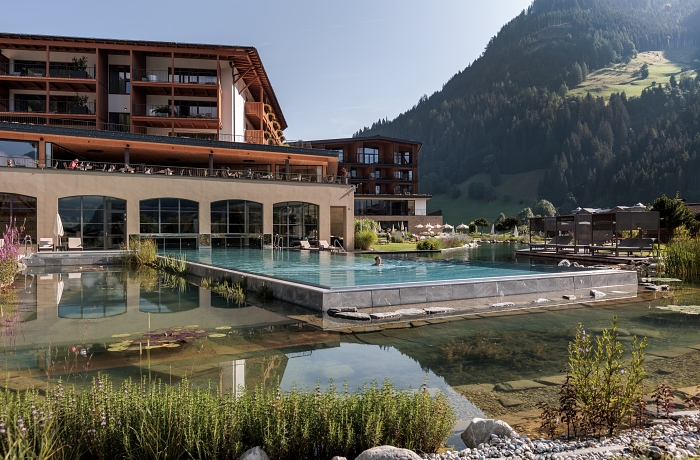 Blick auf das großartige Wellnesshotel Nesslerhof mit Teich, Infinitypool und Hauptgebäude mit vielen Balkonen