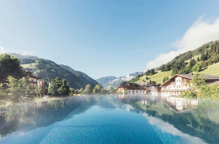 Hauptbild für Blogbeitrag Wellnesshotels Österreich: Außenansicht vom Hotel Nesslerhof mit Pool und Blick in die Berge