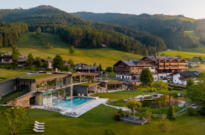 Modernes Alpenresort mit großzügigem Infinity-Pool, Naturbadeteich und weitläufiger Gartenanlage vor einer beeindruckenden Bergkulisse. Die Kombination aus zeitgenössischer Architektur, traditionellen Holzelementen und unberührter Natur schafft eine exklusive Wohlfühlatmosphäre im Herzen der Alpen.