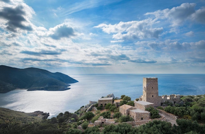 Ruhige Küstenlandschaft mit bewaldeten Hügeln und historischem Steinturm auf einer Anhöhe mit Blick über das Meer.