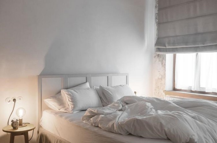 Ein Hotelbett mit weißer Bettwäsche und einem eleganten Nachttisch mit Lampe – so geht Minimalismus.