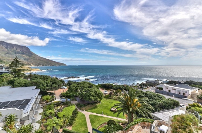 Blick auf die Küste von Kapstadt, davor eine parkähnliche Anlage mit Palmen