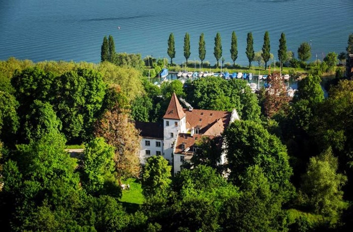 Vogelperspektive auf auf das Schlosshotel umgeben von Bäumen und im Hintergrund ein See