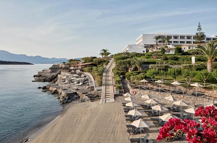 Strandabschnitt mit Steintreppe, Hotel im Hintergrund und vielen Liegen und Schirmen