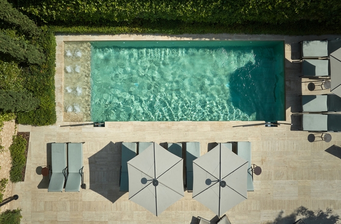 Außenpool aus der Vogelperspektive mit kristallklarem Wasser, stilvollen Sonnenliegen und schattenspendenden Sonnenschirmen. Die minimalistische Gestaltung und die ruhige Umgebung verleihen dem Boutique-Hotel eine exklusive Wellness-Atmosphäre.
