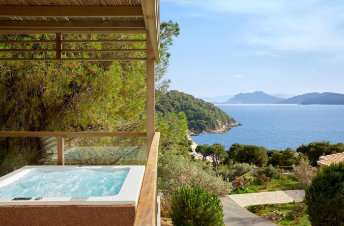 Private Terrasse mit Whirlpool und Holzüberdachung, mit traumhaftem Blick auf eine grüne Küstenlandschaft, das blaue Meer und umliegende Inseln.