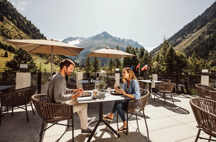 ein Pärchen frühstückt auf der Terrasse mit Panoramablick auf die Berge