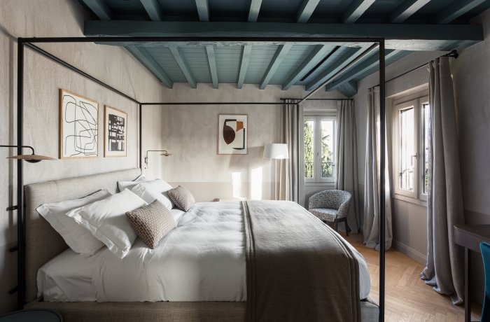Elegantes Hotelzimmer mit Himmelbett, Holzbalkendecke, moderner Einrichtung und großen Fenstern.