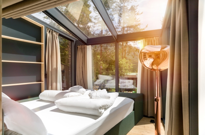Helles Schlafzimmer mit großem Bett unter Glasdach und freiem Blick in die Natur und umliegende Berglandschaft.