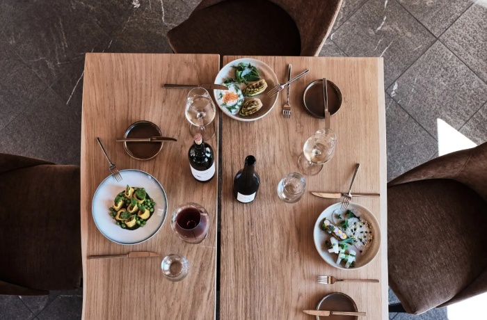 Hotels mit Gourmetrestaurant: Elegant gedeckter Holztisch mit Gourmetgerichten, Weinflaschen und edlem Besteck in einem stilvollen Hotelrestaurant.