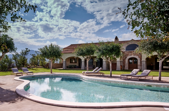 Mediterrane Villa mit stilvollem Außenpool, Natursteinarchitektur und gepflegter Gartenanlage inmitten der Landschaft Sardiniens.