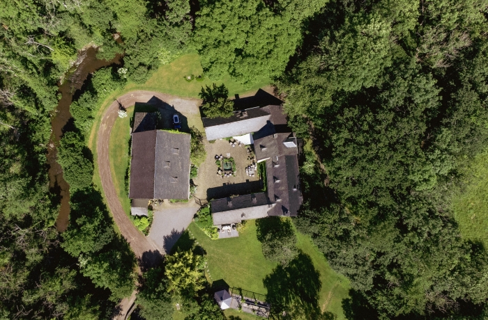 Drohnenaufnahme des Löffelmühle mit Innenhof und mehreren Gebäuden, umgeben von dichtem Wald und einer geschwungenen Zufahrt.