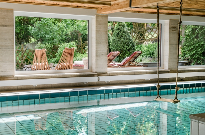 Innenpool mit großen Fenstern, Blick in den Garten und Liegestühlen für entspannte Wellnessmomente.
