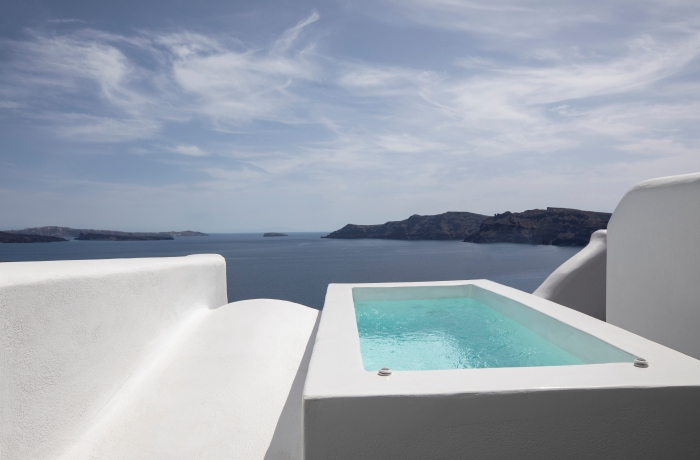Privater Pool auf einer weißen Santorini-Terrasse mit spektakulärem Blick über die Ägäis und die markanten Vulkaninseln am Horizont.