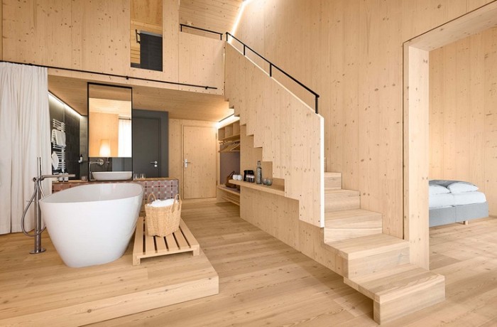Modern gestaltete, doppelstöckige Suite mit heller Holzvertafelung, freistehender Badewanner und gemütlichem Polsterbett.
