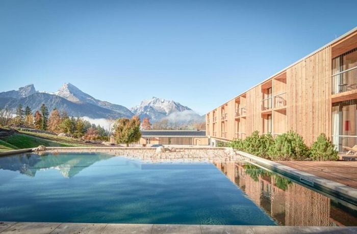 Spektakuläre Pools: Schwimmteich und mit Holz verkleidetes Hotel, im Hintergrund Park und Berge