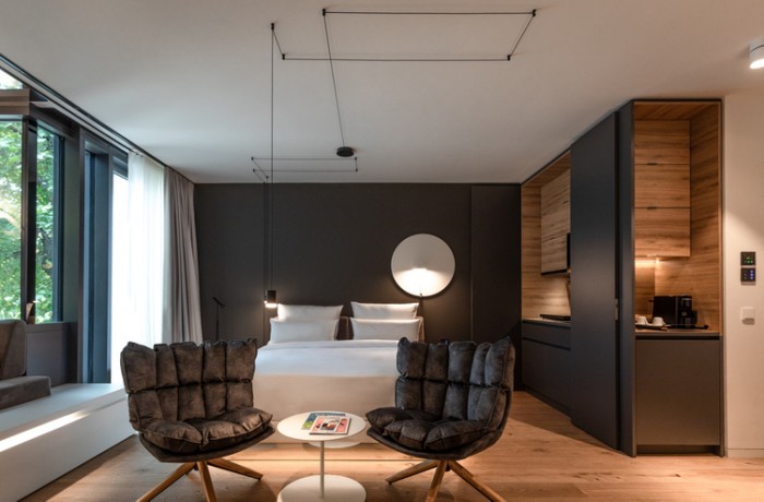 Eines unserer top Designhotels: Dunkles Mobiliar und Polstersessel sowie Wandspiegel und eine Kochnische im KPM Hotel & Residences