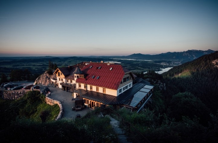 Blick auf das in Höhenlage befindliche Gourmethotel Blaue Burg Falkenstein, das von einer Terrasse sowie einer Zufahrtsstraße umrahmt wird