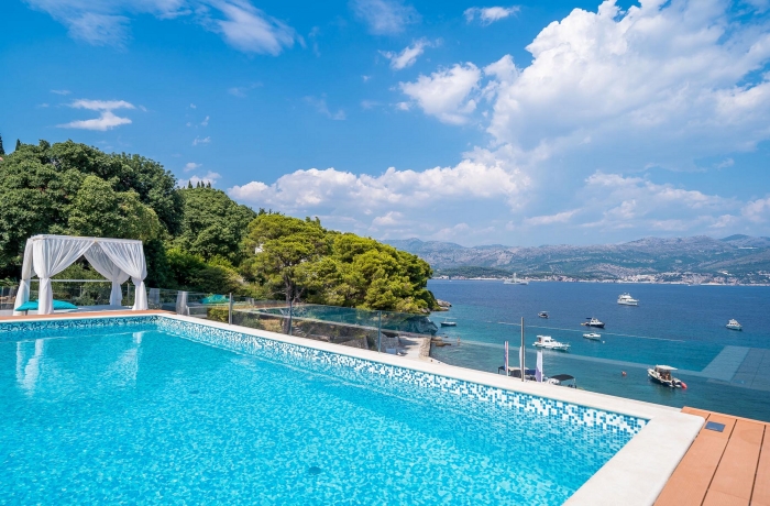 Infinity-Pool mit traumhaftem Meerblick, umgeben von mediterraner Natur, einer stilvollen Lounge-Cabana und kristallklarem Wasser entlang der Küste.