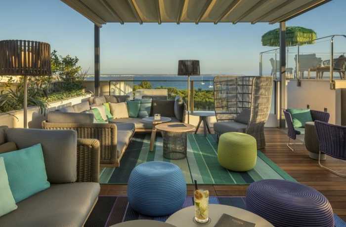 Outdoor-Hotelbar mit grünen und blauen Sitzpoufs, modernen Gartenmöbeln und mit Blick auf das Meer