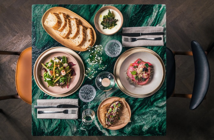 Hotels mit Gourmetrestaurant: Stilvoll gedeckter Tisch mit verschiedenen kreativen Gourmetgerichten, frischem Brot, Salaten und Wasser, auf grün gemusterter Marmorplatte.