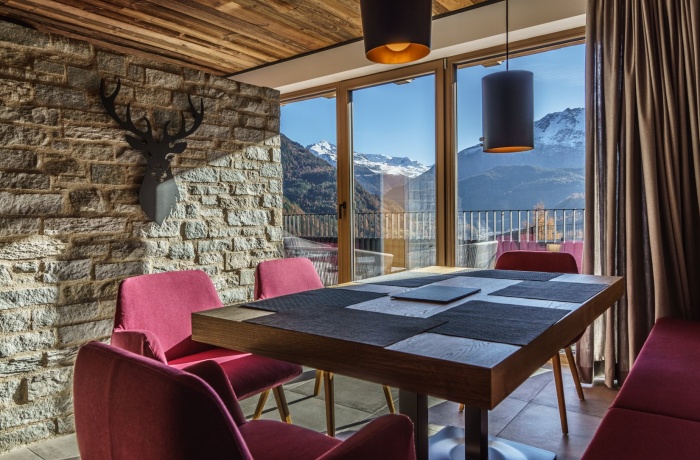 Modernes Esszimmer im The Peak Sölden mit Steinwand, Holzdecke, gemütlichen roten Stühlen und Panoramablick auf schneebedeckte Berge durch große Fenster