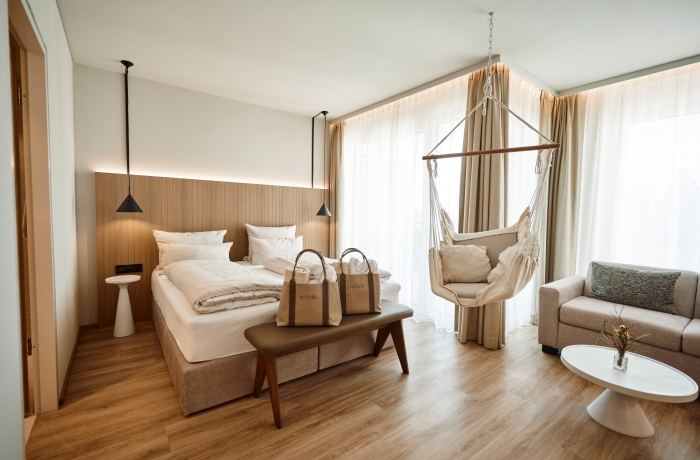 Modernes Schlafzimmer mit Doppelbett, Hängesessel, Sofa und großen Fenstern, hell und stilvoll eingerichtet.