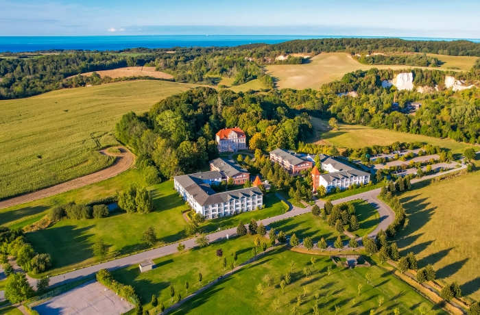 Luftaufnahme eines weitläufigen Resorts inmitten grüner Natur mit Blick auf die Ostsee, umgeben von Feldern, Wäldern und sanften Küstenlandschaften.