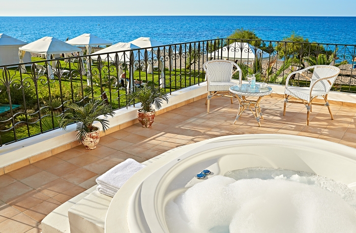 Hotelterrasse mit Whirlpool, Tisch und Stühlen sowie Blick auf das Meer.