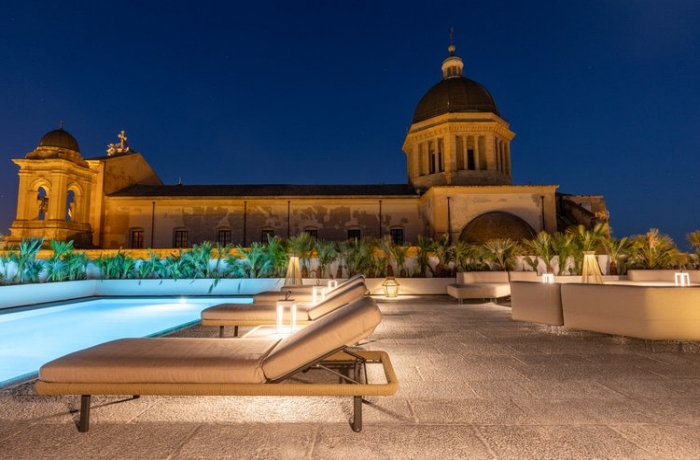 Abendstimmung auf Sizilien: Links der Dachpool, im Hintergrund der Blick auf einen von sieben Domen der Stadt Marsala, gemütlich gepolsterte Sonnenliegen und Loungemöbel laden zum Verweilen ein