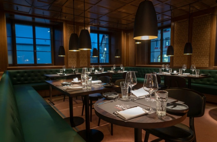 Stilvolles Hotelrestaurant mit dunklem Holzinterieur, grün gepolsterten Bänken, modern gedeckten Tischen und warmem Licht am Abend.