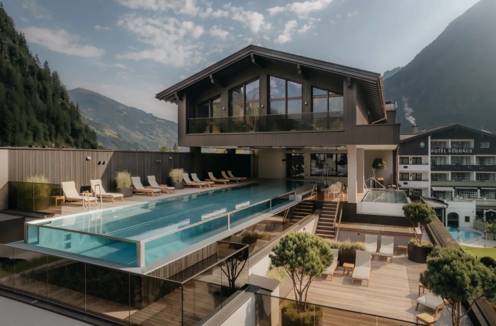 Modernes Berghotel mit einem schwebenden Infinity-Pool auf einer erhöhten Holzterrasse, umgeben von stilvollen Sonnenliegen und Pflanzen. 