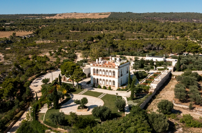 Luftaufnahme eines exklusiven Landresorts mit historischer Villa, gepflegten Gartenanlagen und mediterraner Naturkulisse in ruhiger Alleinlage.