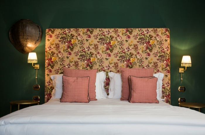 Elegantes Hotelzimmer mit floralem Kopfteil, dunkelgrünen Wänden und stilvollen Designakzenten in warmem, klassischem Ambiente.