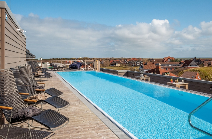 Moderner Rooftop-Pool mit großzügiger Sonnenterrasse und Panoramablick über die Dächer eines Küstenorts bis zur Nordsee am Horizont.