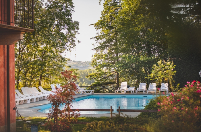Außenpool im grünen Garten eines Agriturismo mit Sonnenliegen und altem Baumbestand – ideal für entspannte Urlaubstage in der Natur.