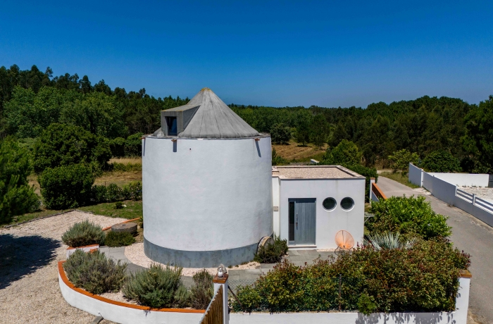 Windmühle mit Garten in ruhiger Umgebung und mediterranem Flair unter klarem Himmel.
