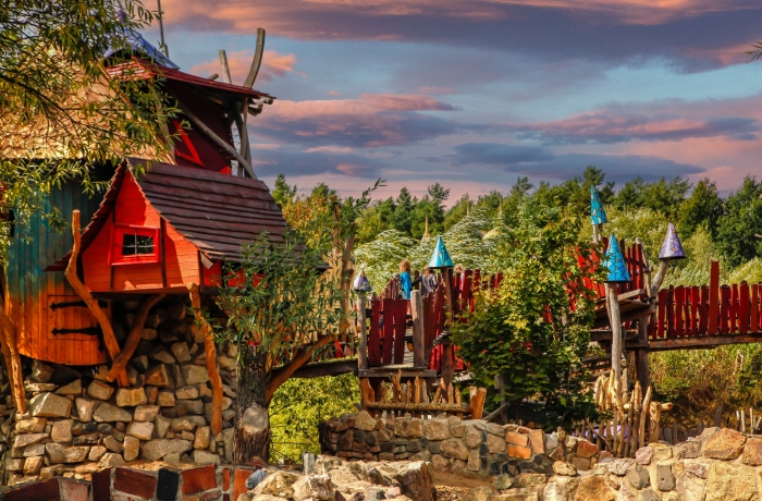 Bunte Baumhausanlage mit kreativen Holzhäusern, Brücken und fantasievoller Gestaltung mitten im Wald.