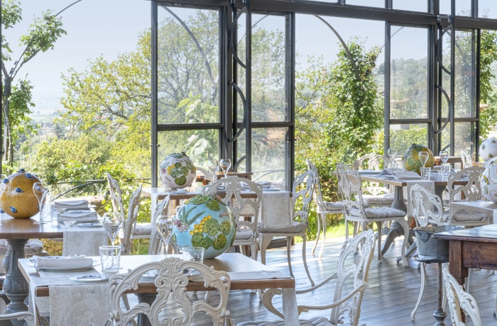 Helles, elegant eingerichtetes Hotelrestaurant mit großen Panoramafenstern, kunstvoll verzierten Stühlen und Blick ins Grüne.