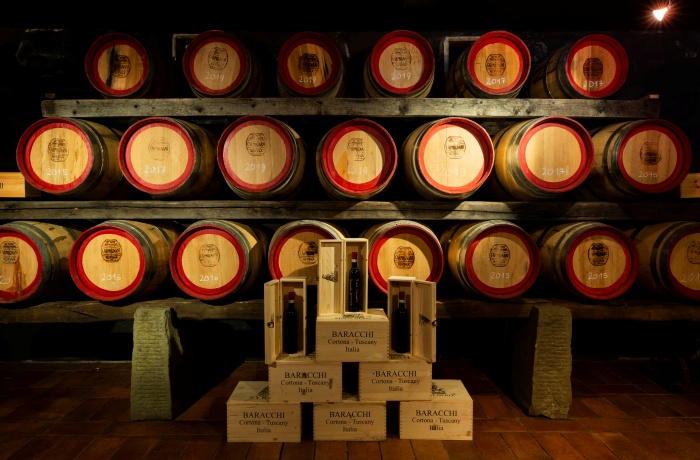 Weingut Hotels: Weinkeller mit gestapelten Holzfässern und dekorativ arrangierten Weinkisten und Flaschen im Vordergrund.
