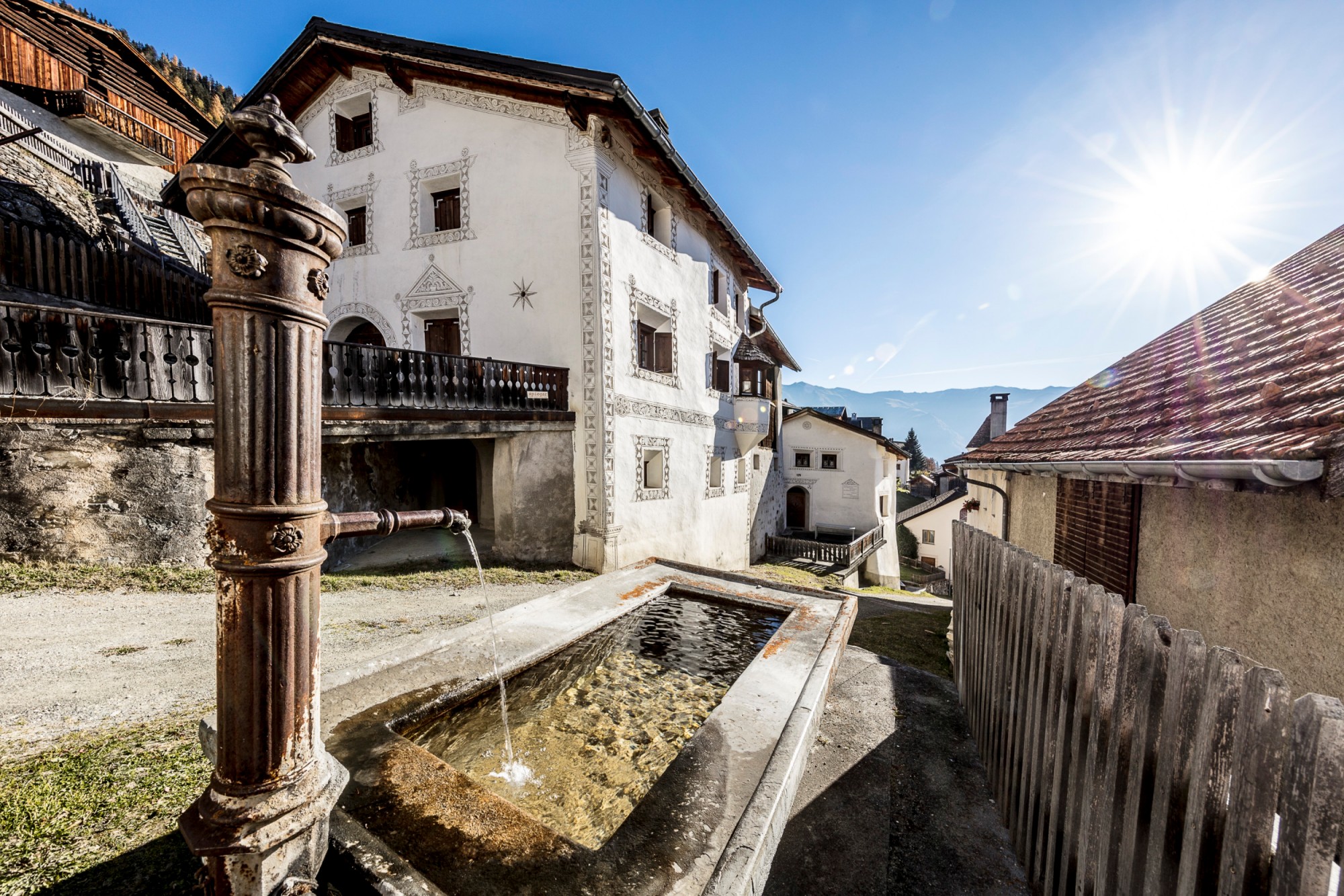 Bemalte Hausfassade und klassischer Steintrogbrunnen im Unterengadin