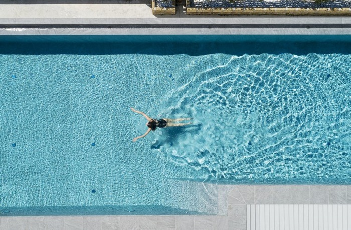 Frau die in einem türkisen Pool schwimmt aus Vogelperspektive
