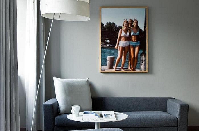 Ausschnitt Hotelzimmer im Sofitel Alter Wall, Hamburg: Mit grauer Couch, Stahlampe und Retro-Bild mit Frauen in Bikinis