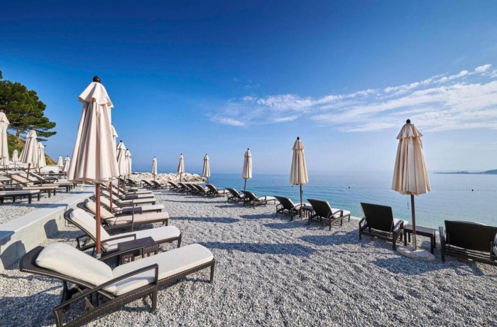 Kiesstrand mit Liegen und Sonnenschirmen