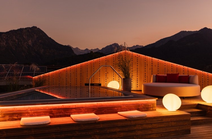 Bild bei fortgeschrittenem Sonneuntergang, warme Sommerstimmung und rotes Licht hängen über dem Sky Onsen Pool des Wellnesshotels Frank in Oberstdorf