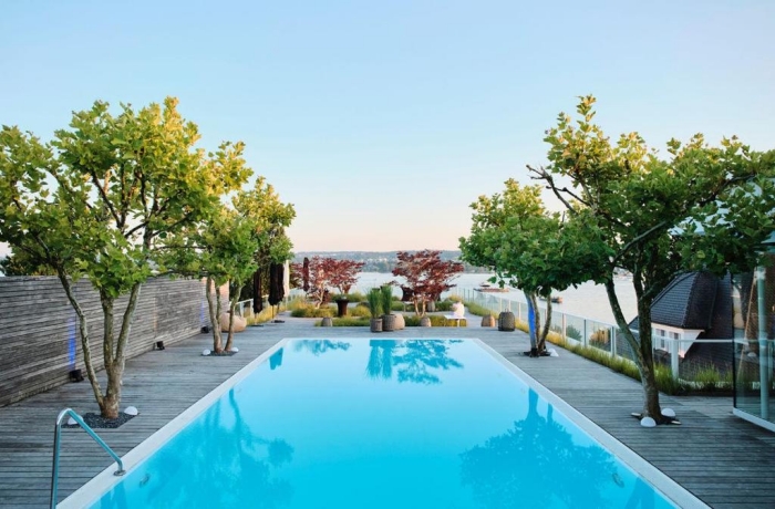 Moderner Außenpool auf einer stilvollen Dachterrasse mit Blick auf den See, umgeben von Bäumen und entspannter Lounge-Atmosphäre.