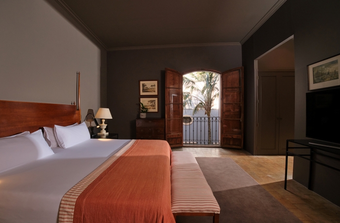 Elegantes Boutique-Hotelzimmer mit klassischem Interieur, hochwertigen Stoffen und französischem Balkon. Die warme Farbgestaltung, edle Holzmöbel und das stilvolle Ambiente verbinden historischen Charme mit modernem Komfort im Herzen von Palma de Mallorca.