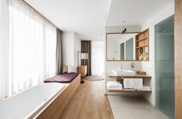 Offen gestaltetes Badezimmer mit hellem Holz, großer Badewanne und lichtdurchfluteter Atmosphäre.