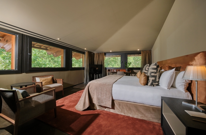 Großzügiges Designzimmer mit modernem Interieur, warmen Naturtönen und großen Fensterflächen mit Blick ins Grüne. Die stilvolle Einrichtung und die ruhige Atmosphäre schaffen einen exklusiven Rückzugsort im Zentrum von Palma de Mallorca.