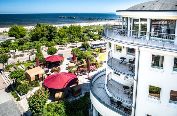 Ein Hotelgebäude steht hinter einer parkähnlichen Anlage am Strand